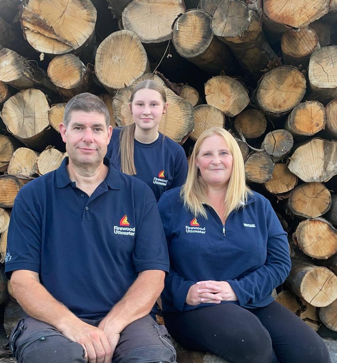 Lee, Lauren and family in front of a stack of logs